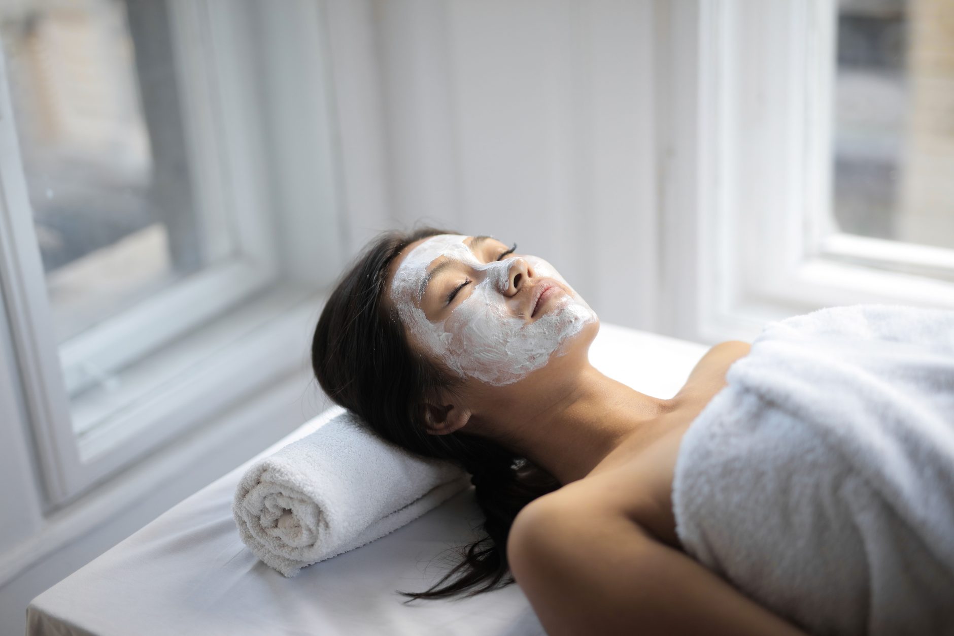A client resting during a facial treatment beside a bright window